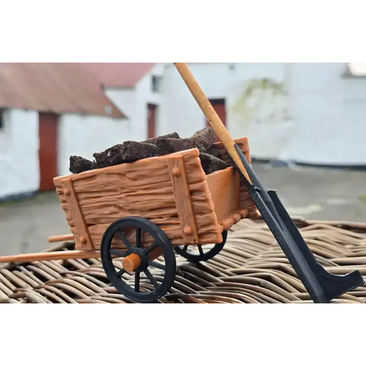 Miniature turf cart filled with turf sods and a turf spade, on wicker with white cottages behind
