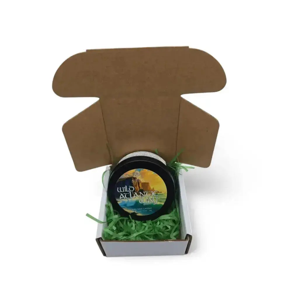 Wild Atlantic Way candle tin in an open brown mailer box with green paper shred