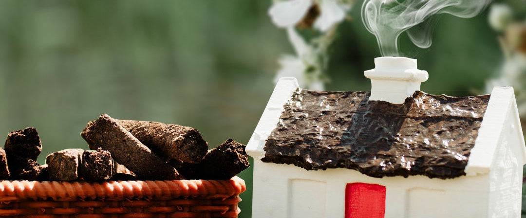 Small house-shaped incense burner with smoke emitting from it, next to a basket of incense sticks and white flowers.