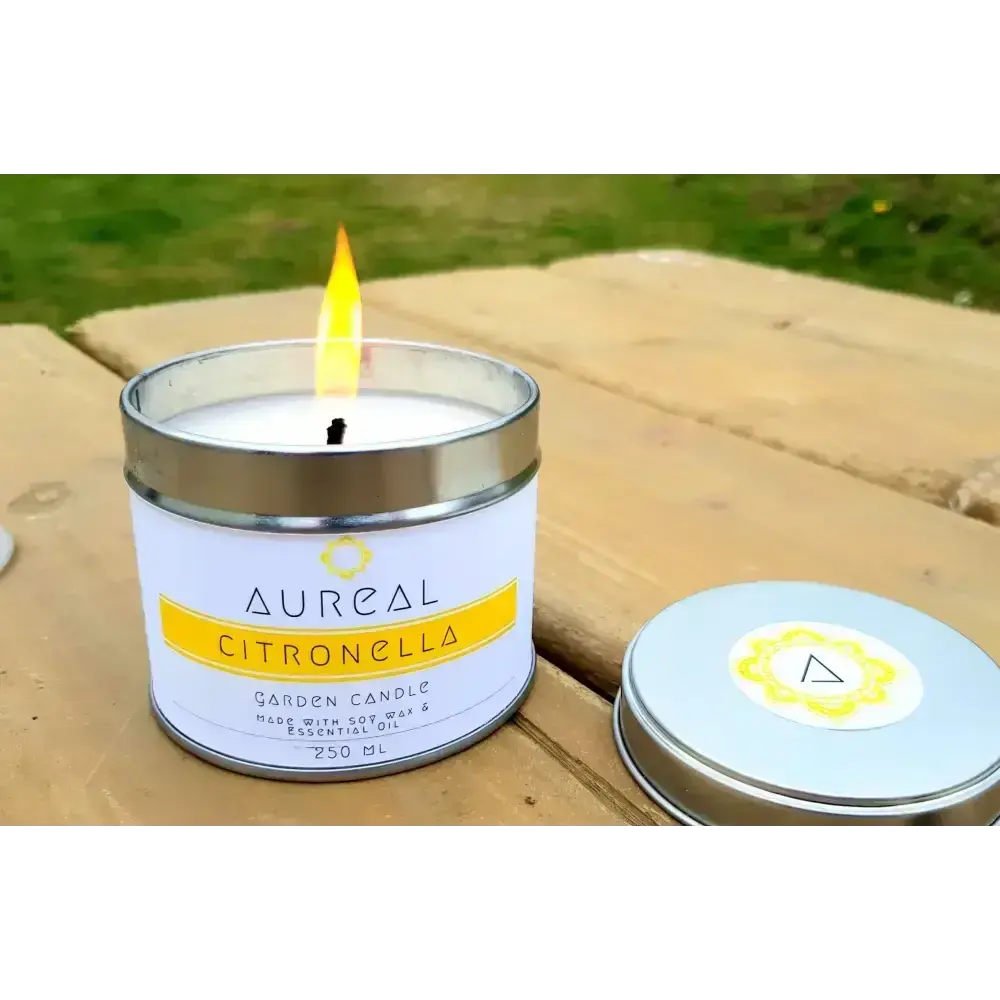 Lit Aureal Citronella garden candle in a tin on a wooden picnic table, lid beside it