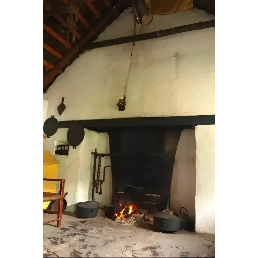 Old cottage hearth with a small open fire, pots and a whitewashed chimney breast
