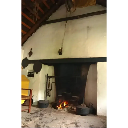 Old cottage hearth with a small open fire, pots and a whitewashed chimney breast