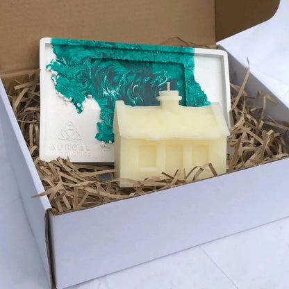 Irish cottage candle and its white and green base in an open box with paper shred