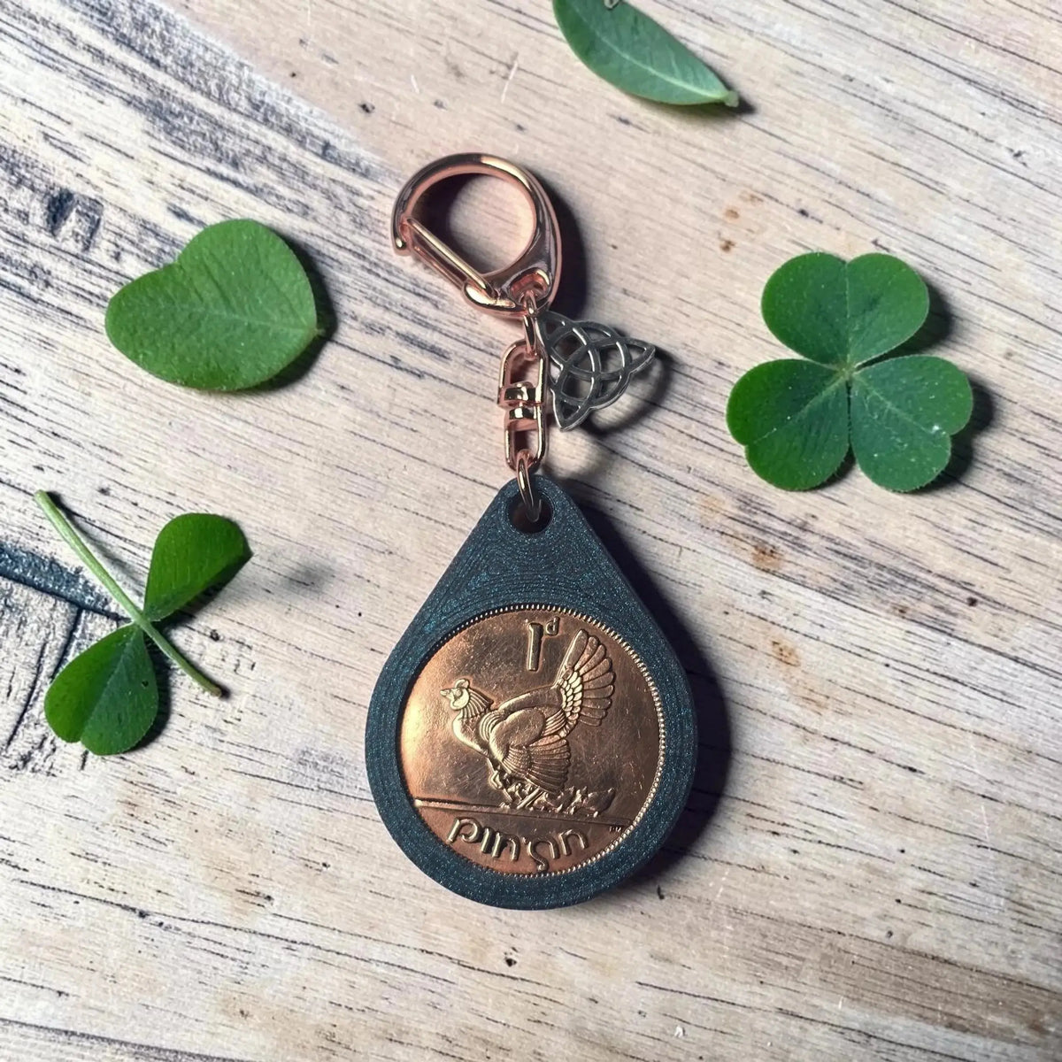 Irish penny keyring showing the hen side, with shamrock leaves on a wooden table