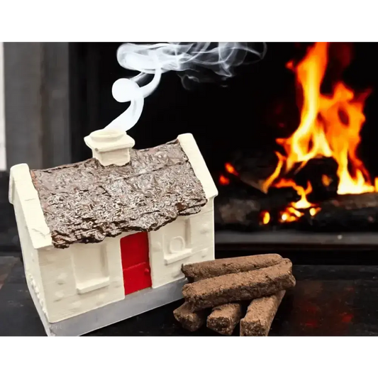 White cottage burner with smoke rising from the chimney, turf sods beside it and a fire behind