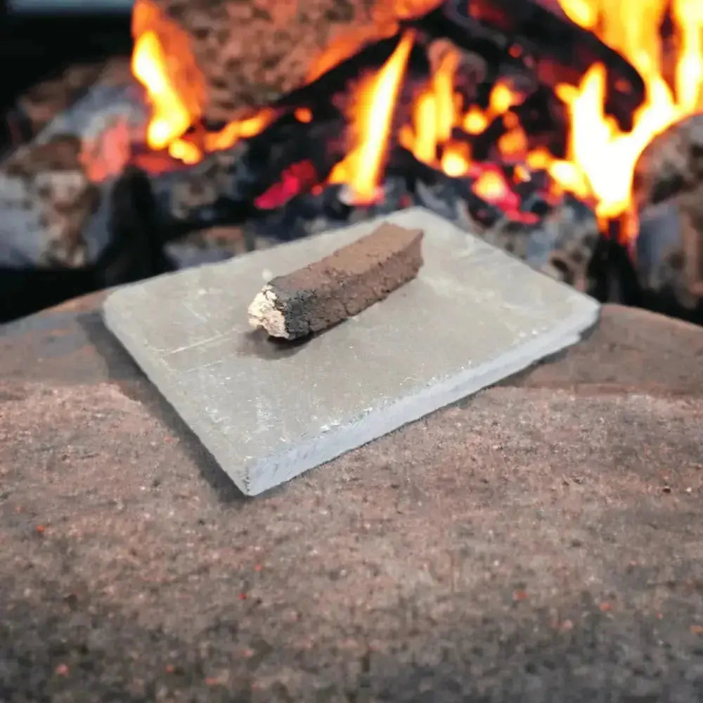 One turf incense sod with a burnt, ashy end on a grey slate, with a fire in the background