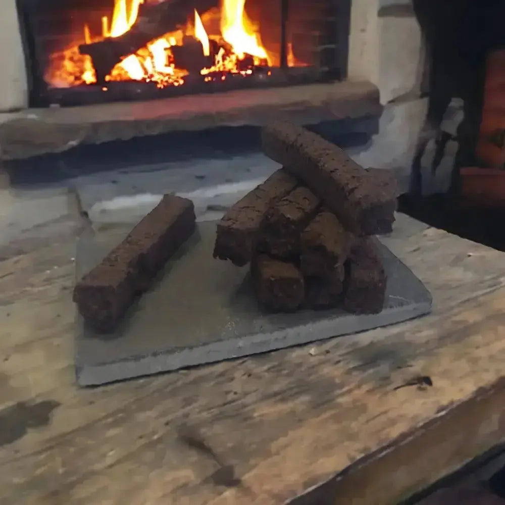 Turf incense sods stacked on a slate on a wooden table, with a lit fire behind