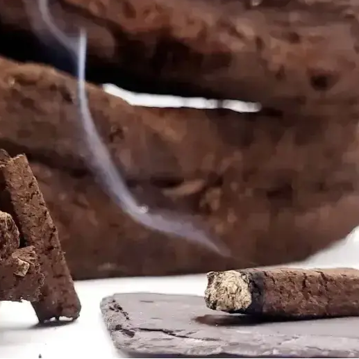 Close up of a turf incense sod smouldering on dark slate, with thin smoke rising