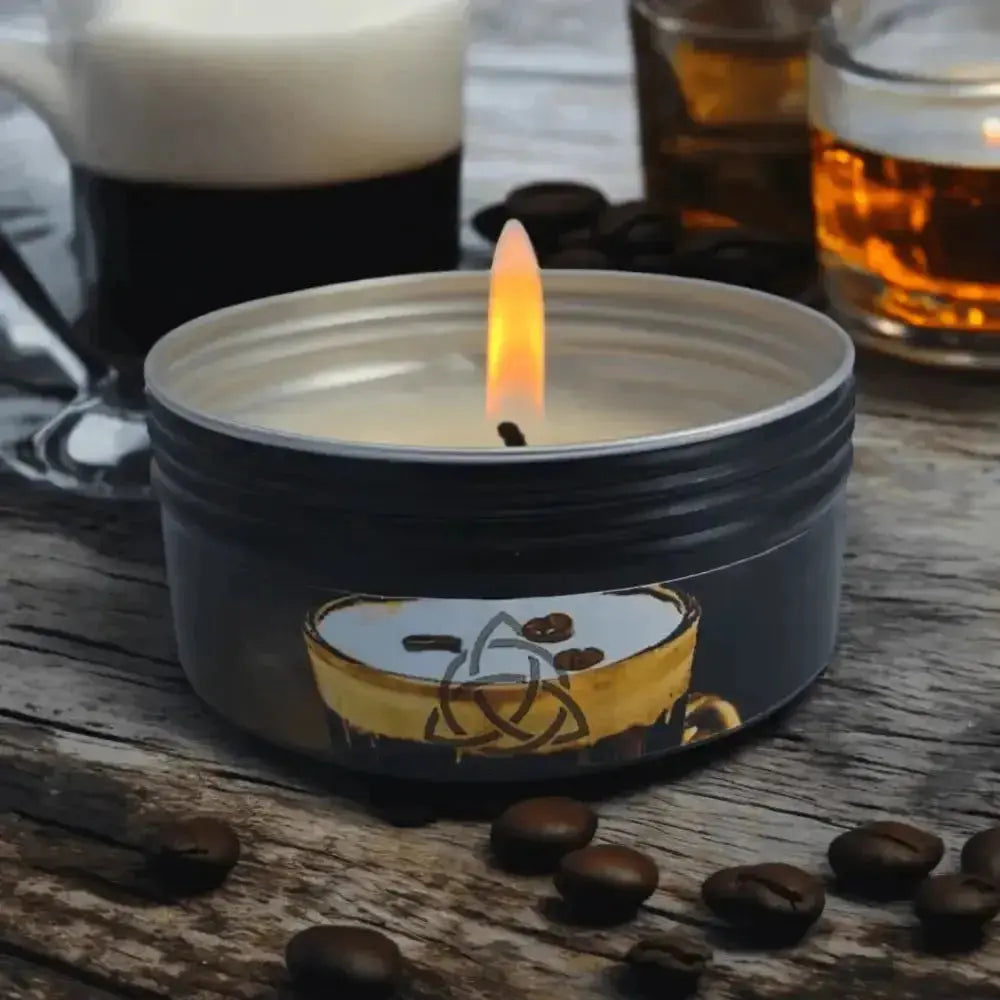 Lit black tin candle with a coffee cup label on wood, coffee beans and glasses behind