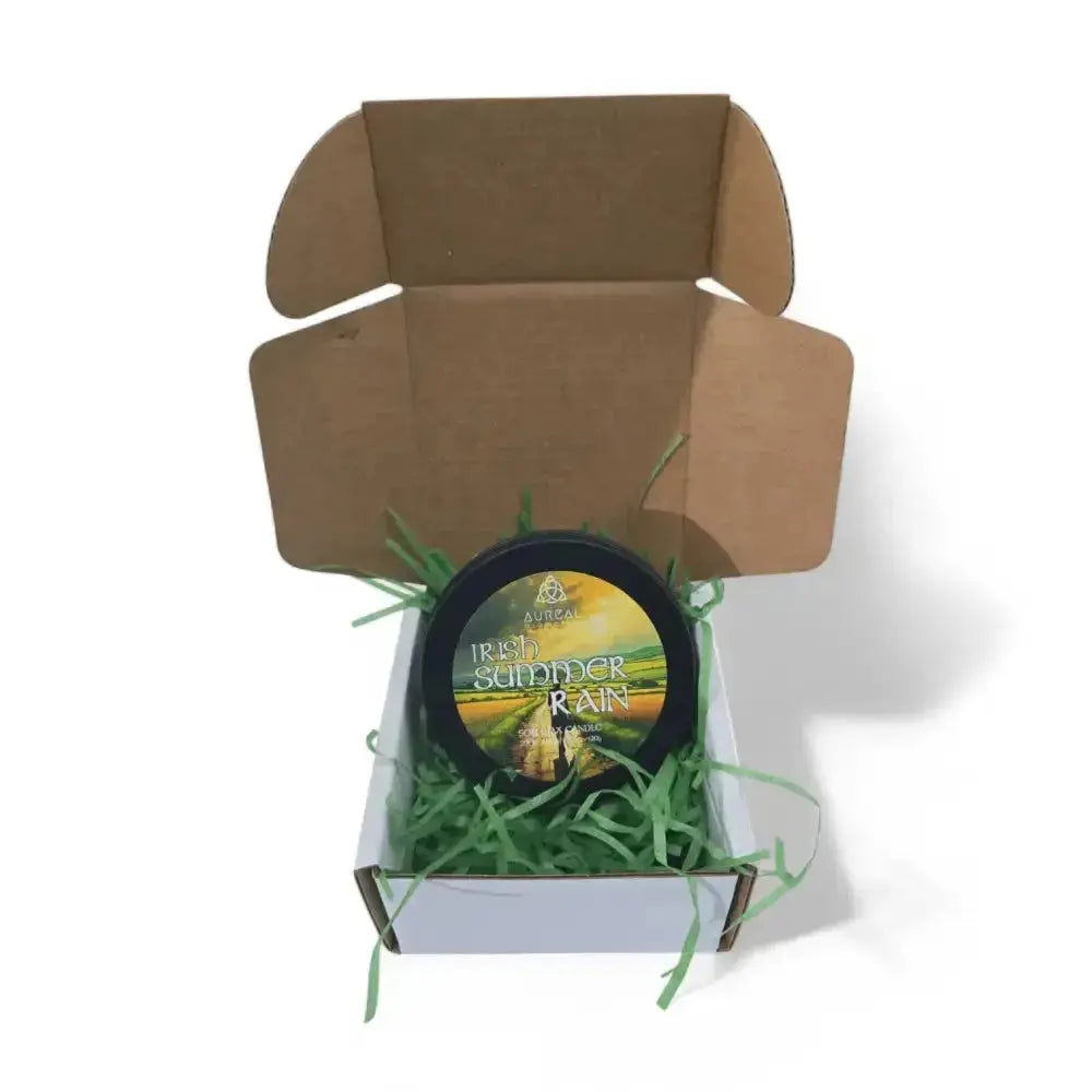 Irish Summer Rain candle tin in an open brown mailer box with green paper shred