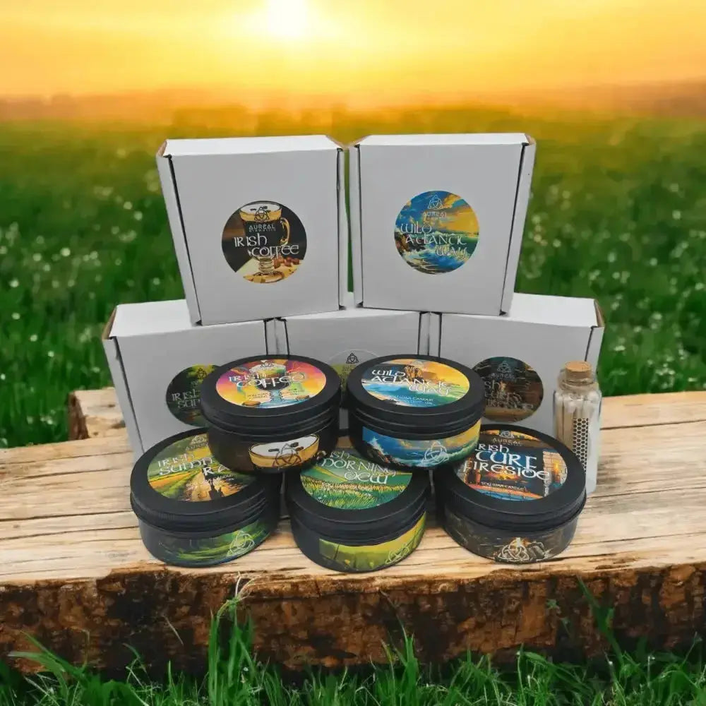 Five candle tins and a bottle of matches in front of their white boxes, on wood in a sunlit field