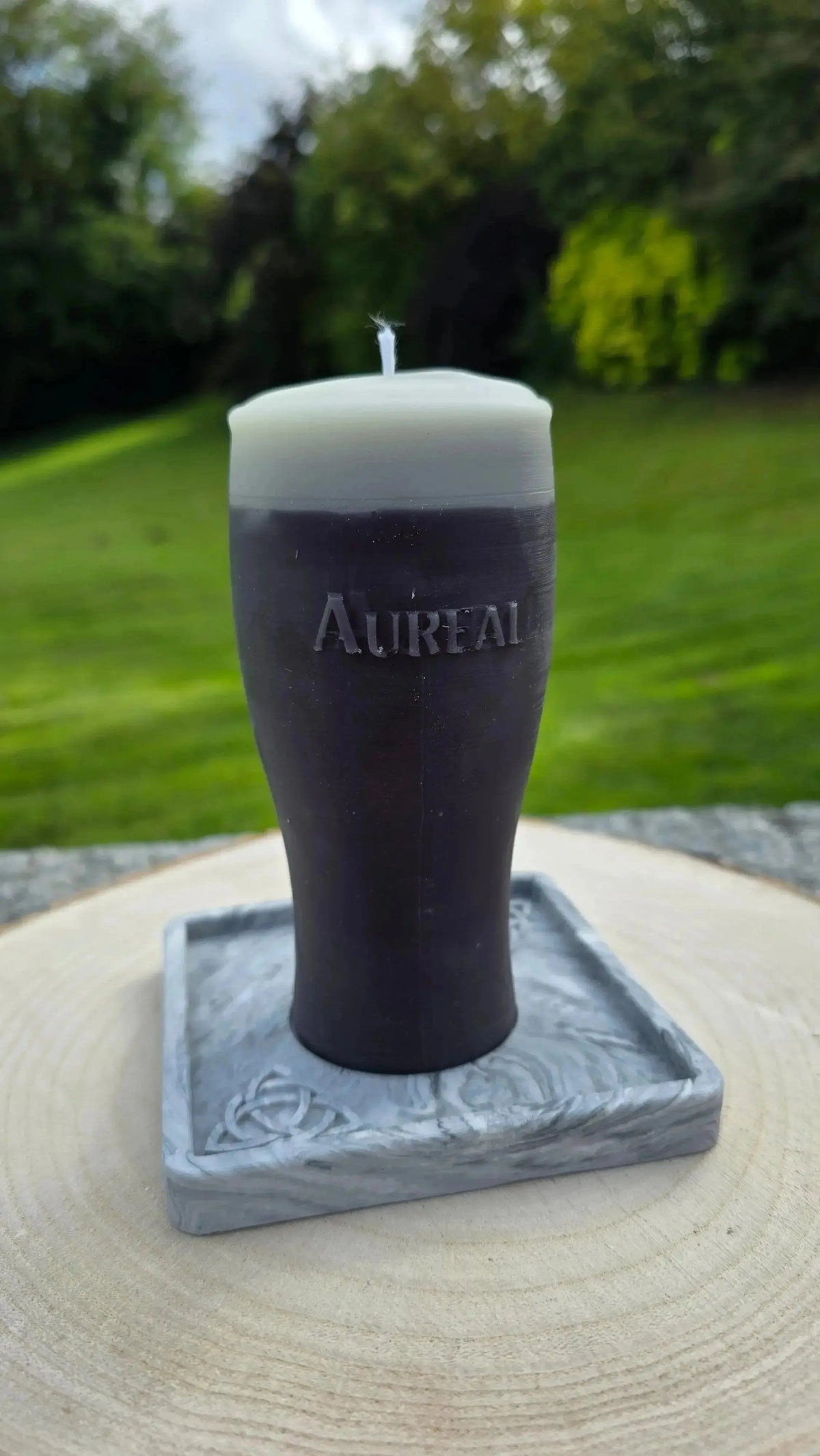 Pint of stout candle on a square marble effect base on a wood slice outdoors