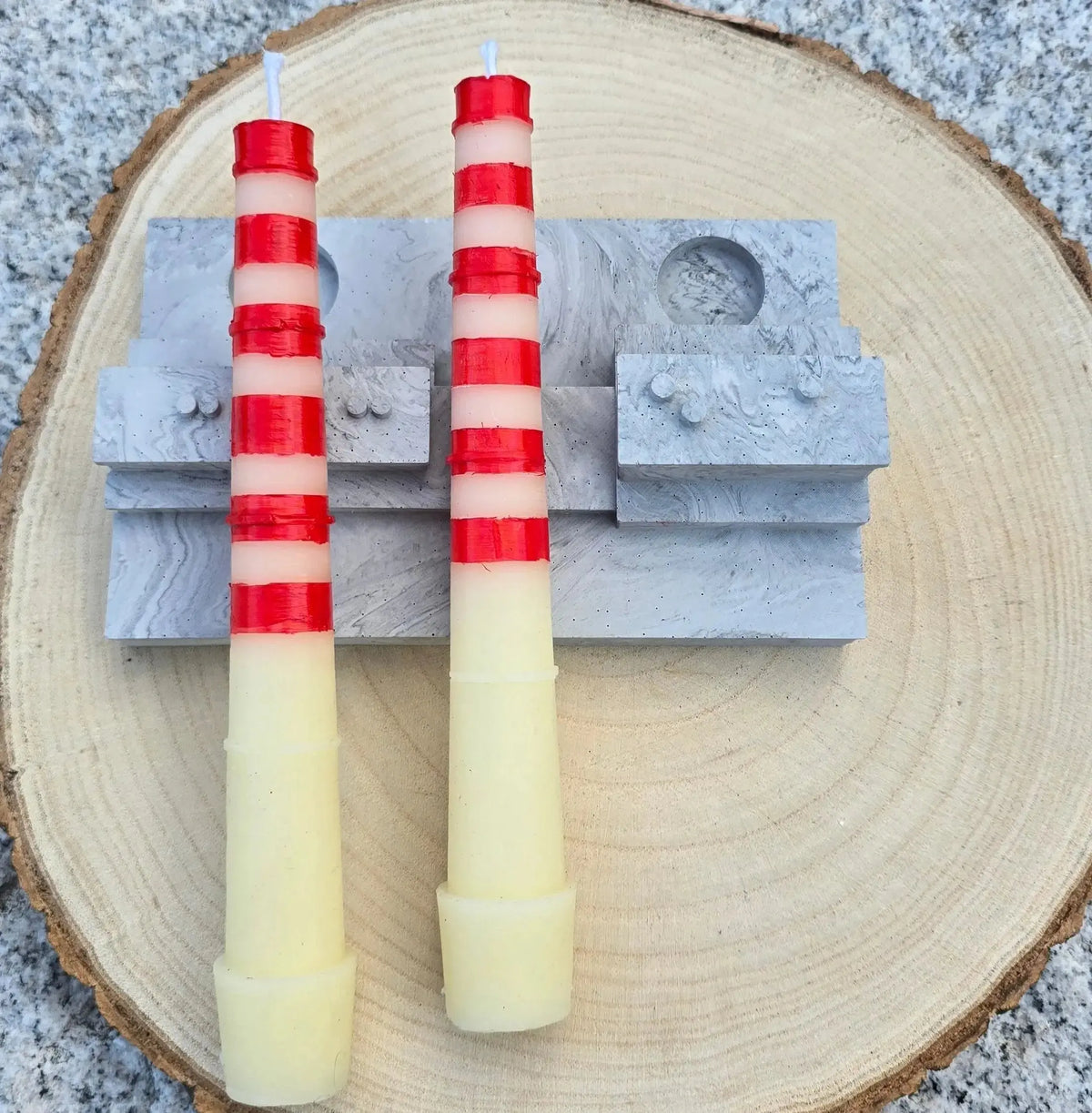 Two red and white striped Poolbeg chimney candles lying on their grey stone effect base
