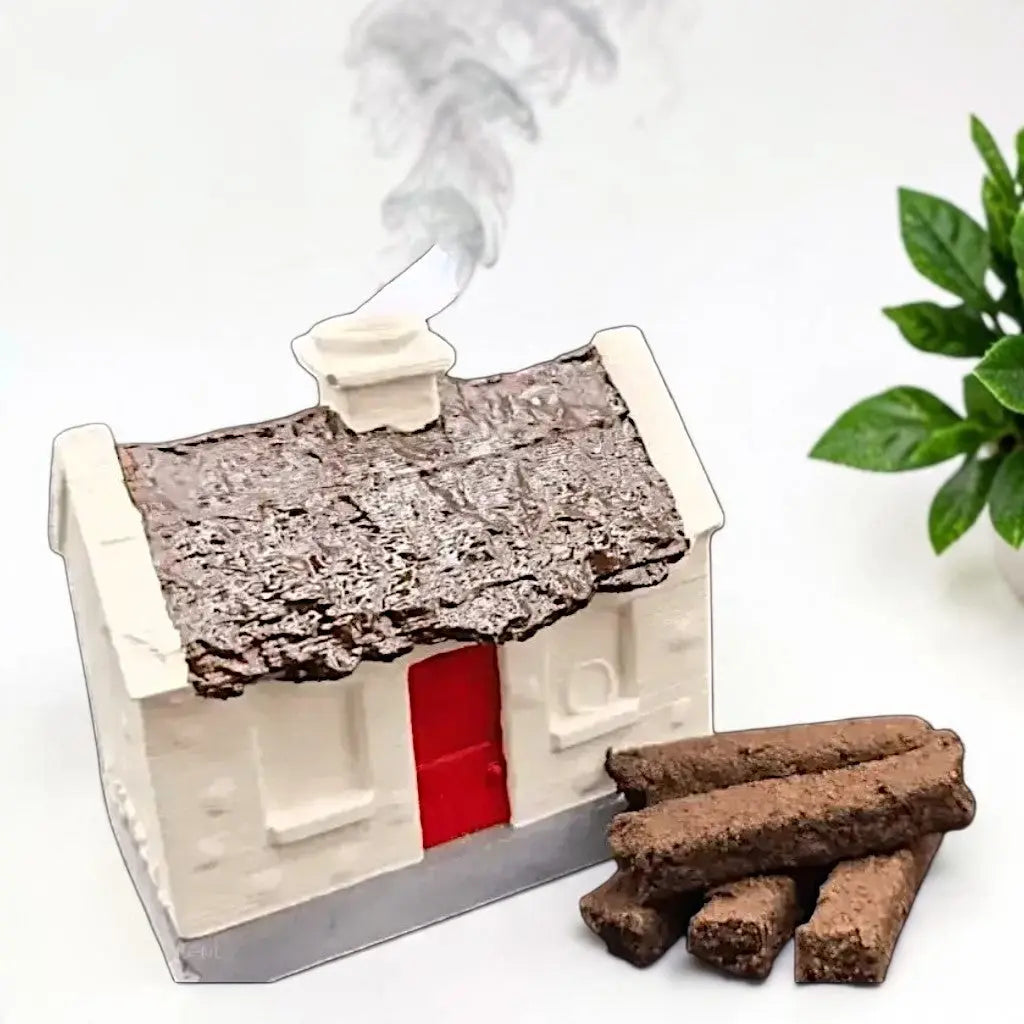 White cottage burner with a brown roof and red door, smoke from the chimney, turf sods stacked beside it