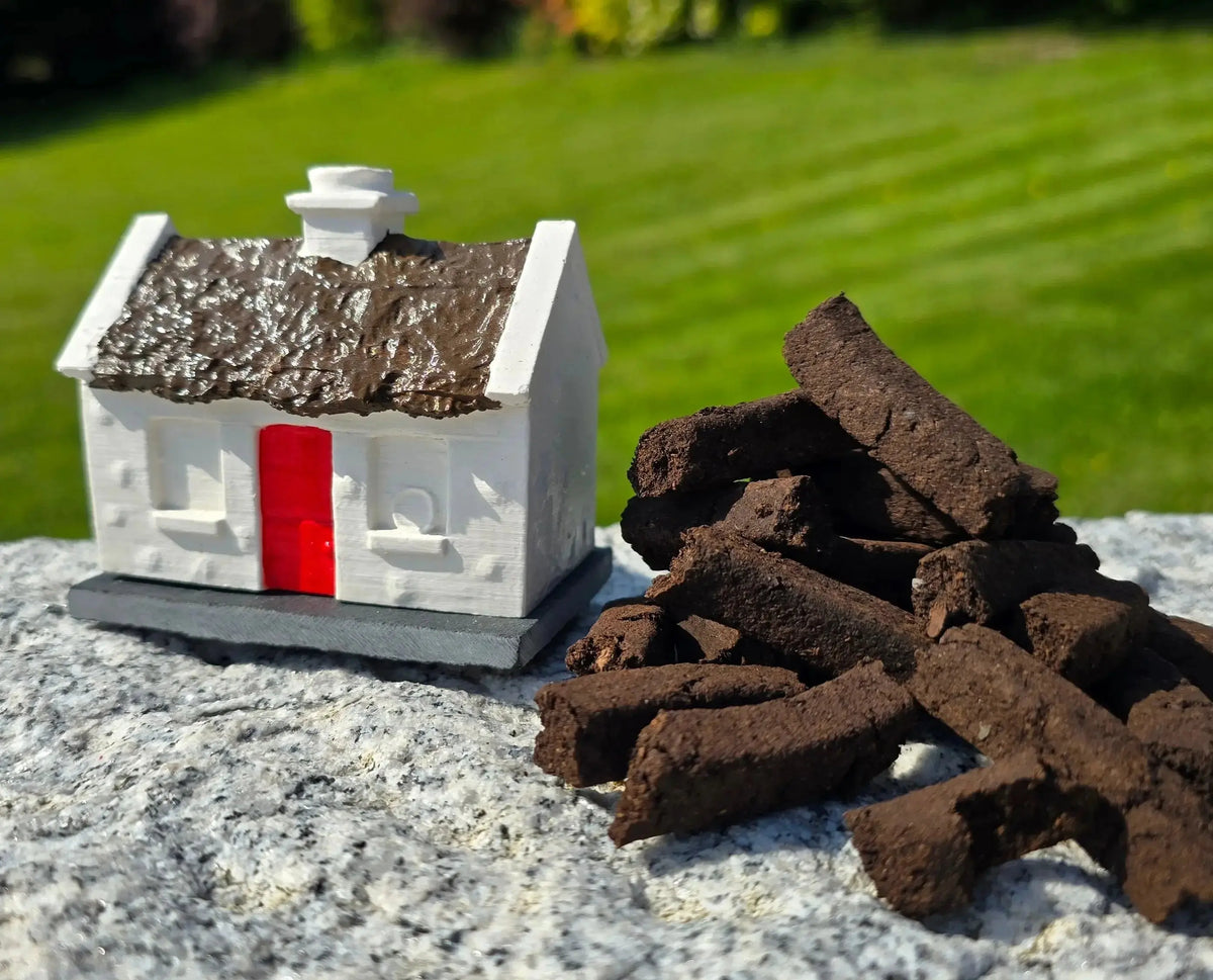 White cottage burner with a red door on a slate beside a pile of turf sods, outdoors on stone